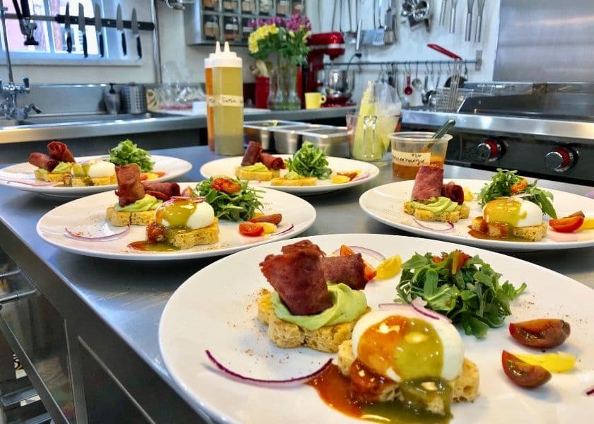 A series of elegantly plated breakfast dishes featuring poached eggs, greens, tomatoes, and crispy bacon in a kitchen setting. A series of elegantly plated breakfast dishes featuring poached eggs, greens, tomatoes, and crispy bacon in a kitchen setting.